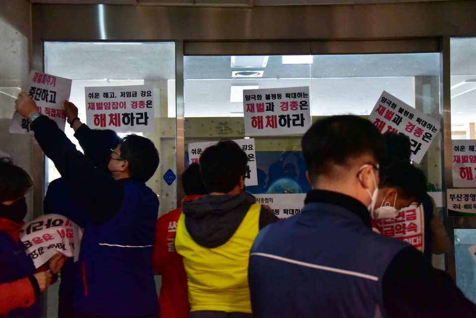 불을 꺼도 햇살이 환히 들어오는 부산 경총 문 앞에 민주노총 부산본부 대표자들이 항의와 요구를 담은 손 구호판을 붙이고 있다.