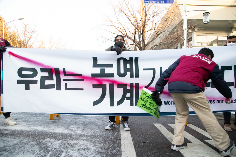 우다야 라이 이주노조 위원장과 차민다 성서공단노조 부위원장이 청와대 앞 마무리 집회에서 ‘우리는 노예/기계가 아니다’라고 씌인 현수막에 X표시를 하는 퍼포먼스를 하고 있다. ⓒ 송승현 기자